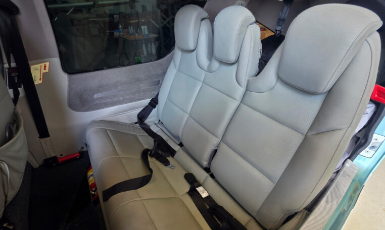 Private plane interior with light gray leather rear bench seats, seat belts, and clean cabin upholstery.