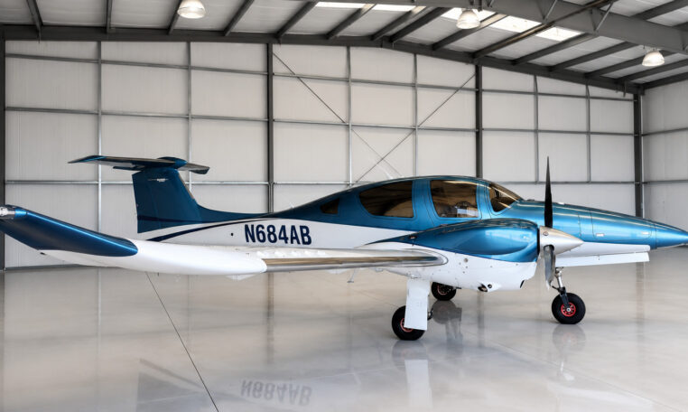 Blue and white single-engine propeller airplane parked in a clean aircraft hangar, tail number N684AB