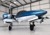 Sleek blue and white twin‑engine propeller airplane parked in a clean aircraft hangar, private plane ready for flight.