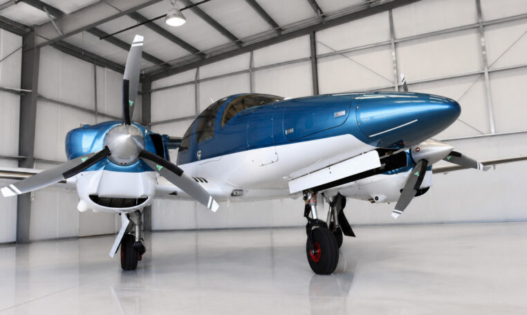 Sleek blue and white twin‑engine propeller airplane parked in a clean aircraft hangar, private plane ready for flight.