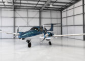 Modern twin-engine propeller aircraft in blue and white parked inside a bright private hangar
