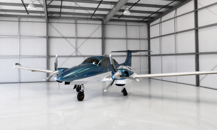 Modern twin-engine propeller aircraft in blue and white parked inside a bright private hangar
