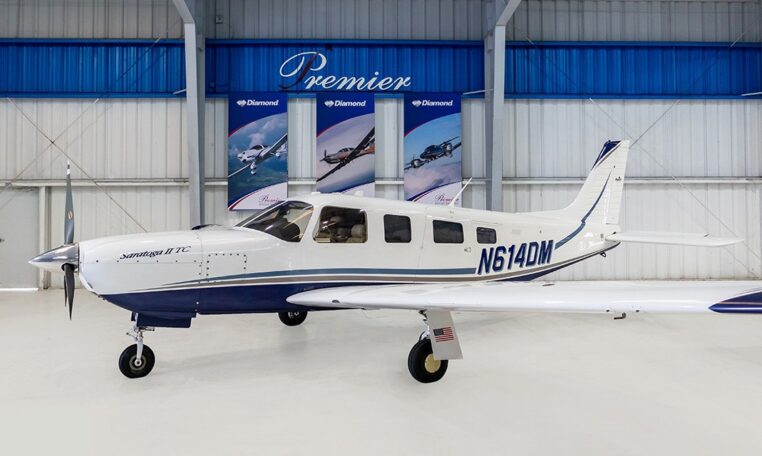 Piper Saratoga II TC N614DM single-engine aircraft in hangar at Premier, side view of blue-white plane.