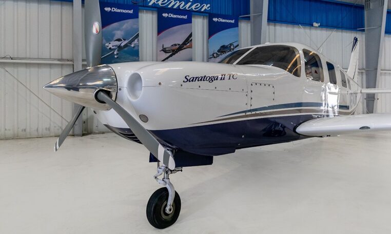 Piper Saratoga II TC single-engine propeller airplane parked in hangar, close-up nose and cockpit view.