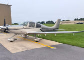 Silver Cirrus SR22 single-engine airplane parked on tarmac at small airport, general aviation aircraft side view.