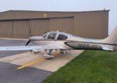 Silver Cirrus SR22 single-engine propeller plane N46JG parked on airport ramp beside hangar.