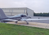 Cirrus SR22 single-engine airplane parked on the ramp near a hangar, private light aircraft on overcast day.
