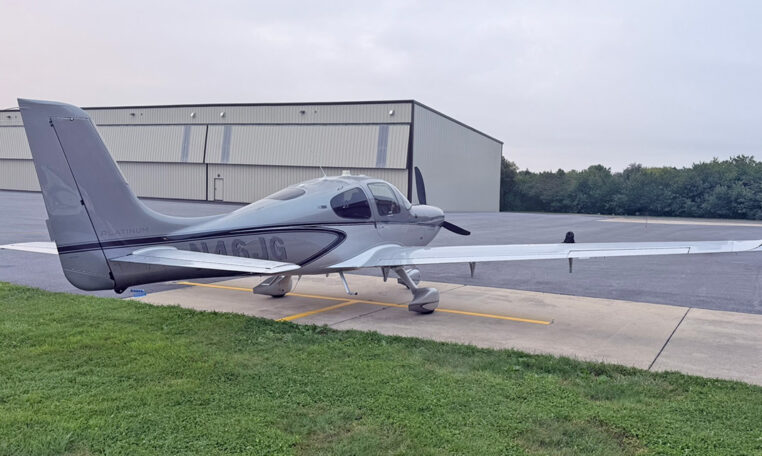Cirrus SR22 single-engine airplane parked on the ramp near a hangar, private light aircraft on overcast day.