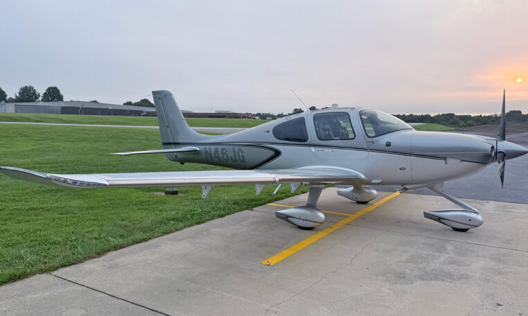 Silver Cirrus single-engine airplane parked on airport ramp at sunrise, tail number N46JG.