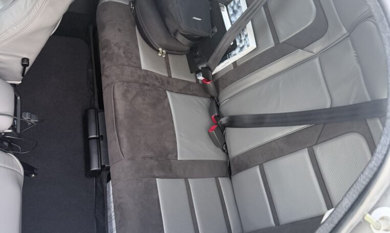 Clean gray and black leather car backseat with seat belts, two-tone rear bench in compact coupe, small bag on seat.