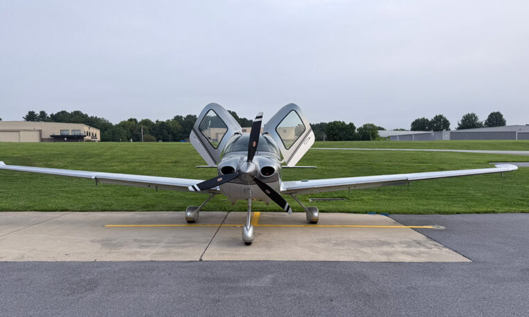 Cirrus SR22 parked on airport ramp, front view with open gullwing doors and three-blade propeller