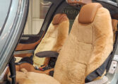 Luxury helicopter cabin with tan leather pilot seats featuring sheepskin covers, center console and seat belts visible.