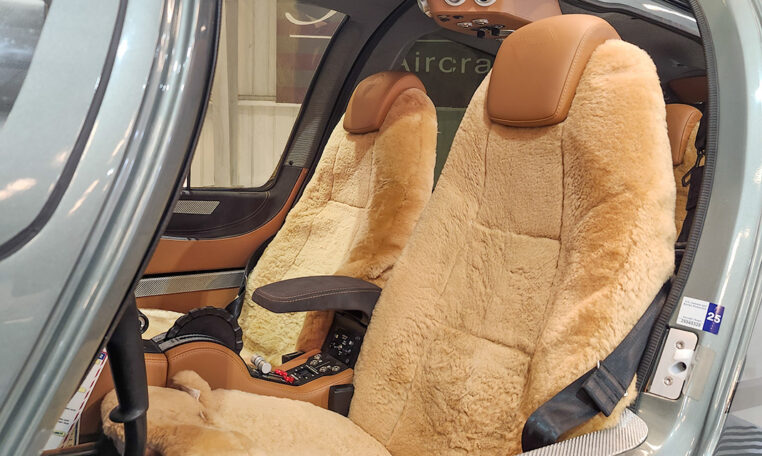 Luxury helicopter cabin with tan leather pilot seats featuring sheepskin covers, center console and seat belts visible.