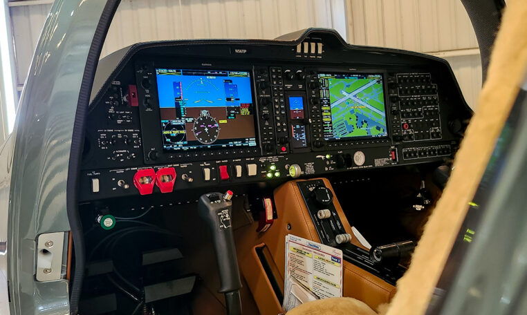 Modern glass cockpit avionics with dual Garmin displays in a general aviation aircraft instrument panel inside a hangar.