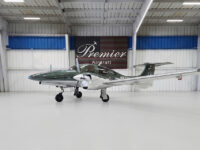 Green and white twin‑engine propeller plane inside Premier Aircraft hangar