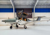 Twin-engine light aircraft with gullwing doors open in a hangar, showcasing tan leather interior and sleek silver finish.