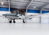 Modern twin-engine propeller airplane in hangar with gullwing doors open, private aircraft ready for flight