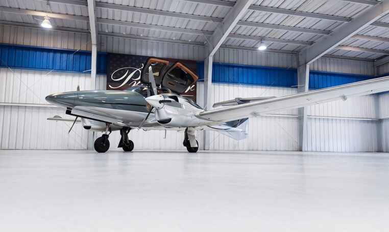 Modern twin-engine propeller airplane in hangar with gullwing doors open, private aircraft ready for flight